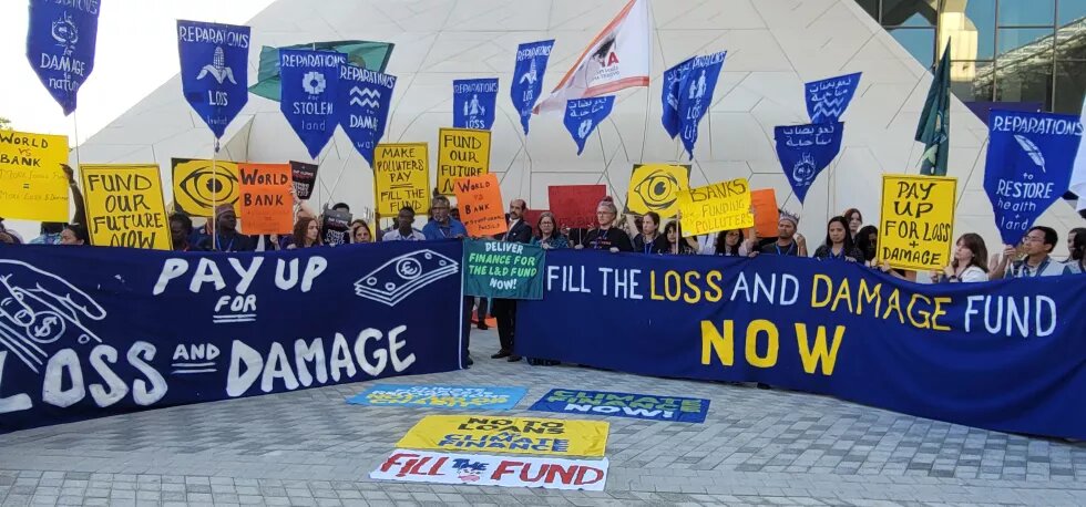 protest at COP28, protestors holding many signs and banners demanding loss and damage funding